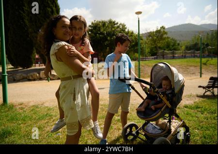 Una famiglia trascorre del tempo di qualità in un parco. Una madre tiene il suo bambino mentre gli altri si godono la giornata. Foto Stock