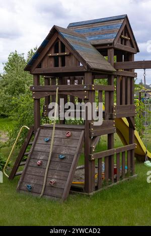 Parco giochi in legno per bambini con parete da arrampicata, corda e scivolo in un giardino sul retro in una giornata nuvolosa, promuovendo un gioco attivo all'aperto e la creatività Foto Stock