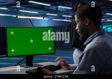 Amministratore del data center che esegue i test diagnostici del sistema utilizzando il display del computer con schermo verde. Lavoratore nella sala server che distribuisce utility di controllo degli errori su PC desktop Chroma Key per riparare i problemi di rete Foto Stock