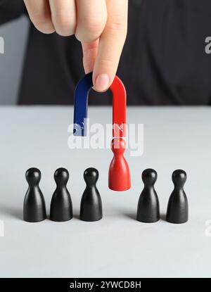Donna con magnete che attrae pezzi rossi tra quelli neri al tavolo bianco, primo piano Foto Stock