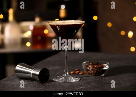 Bicchiere con deliziosi martini espresso, chicchi di caffè e jigger sul tavolo del bar Foto Stock