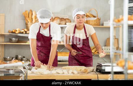 Due giovani fornai che lavorano con l'impasto in un'accogliente panetteria Foto Stock