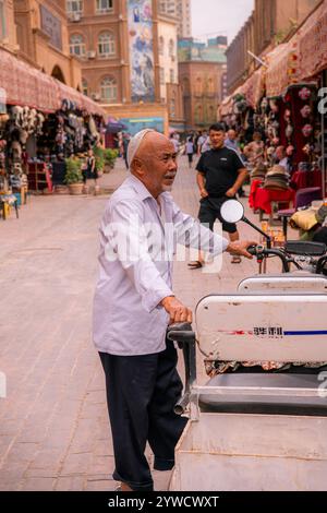 Kashgar, Cina - 17 LUGLIO 2022: Uomo uiguro circondato da tradizionali negozi di cappelli uiguri in un mercato locale nella vecchia Kashgar Foto Stock