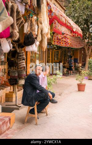 Kashgar, Cina - 17 LUGLIO 2022: Uomini uiguri seduti nel loro tradizionale negozio di cappelli uiguri in un mercato locale nella vecchia Kashgar Foto Stock