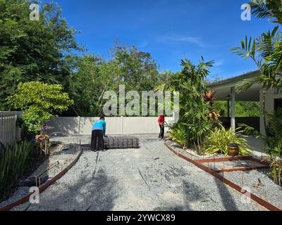 Pattaya, Tailandia 29 novembre 2024, due lavoratori sono impegnati a stendere materiali per il cemento da bollo in una lussureggiante area verde il vibrante paesaggio esalta l'atmosfera di questo progetto all'aperto. Foto Stock