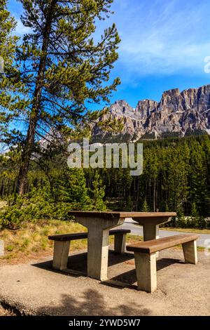 Un tavolo da picnic in legno si trova in un parco vicino a una montagna. Il tavolo è vuoto e il cielo è limpido e blu. La scena è tranquilla e serena Foto Stock