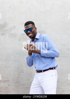 Ritratti allegro giocoso uomo afroamericano sorridente nei suoi 40 anni con occhiali da sole e camicia blu. Ritratto di un uomo felice ed elegante del Medioevo, Gray Foto Stock