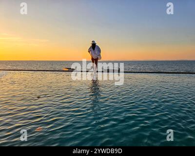 Mentre il sole tramonta sull'isola di Koh Munnork, una figura cammina lungo il bordo dell'acqua, crogiolandosi nelle tonalità dorate del crepuscolo. L'atmosfera tranquilla invita alla riflessione e alla tranquillità. Foto Stock