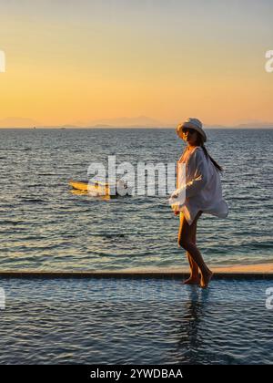 Una serena serata sull'isola di Koh Munnork dove una persona cammina a piedi nudi lungo il bordo dell'acqua, riflettendo le vibranti sfumature di un tramonto mozzafiato. Foto Stock