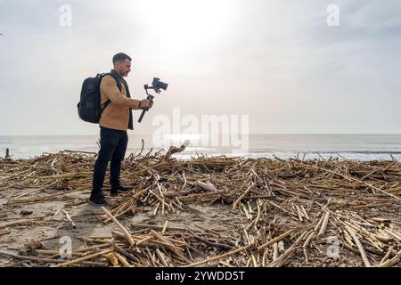 Il videografo cattura pioggia, inondazioni e inondazioni che causano il lavaggio della spazzatura e dei detriti naturali sulla spiaggia Foto Stock
