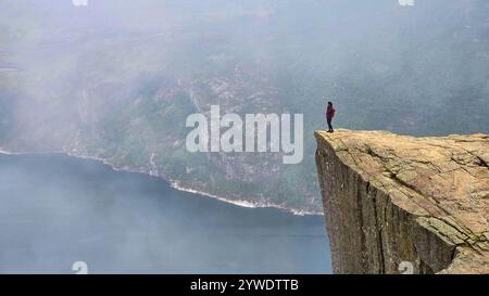 Un escursionista solitario gode di vedute mozzafiato dal bordo di Preikestolen, circondato da nebbia e tranquilli fiordi. Lysefjorden Norvegia Foto Stock