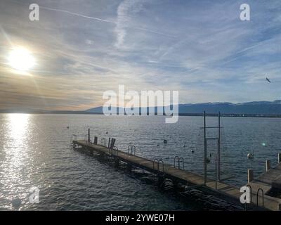 Splendido tramonto sulle acque calme con un molo di legno e montagne lontane in una giornata tranquilla Foto Stock