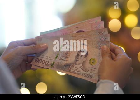 Cina. 11 dicembre 2024. In questa illustrazione, una persona tiene in mano banconote thailandesi Baht con una luce di Natale sullo sfondo. (Foto di Serene Lee/SOPA Images/Sipa USA) credito: SIPA USA/Alamy Live News Foto Stock