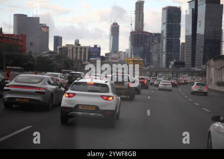 Ayalon Highway, Tel Aviv, traffico intenso in una giornata buia e nuvolosa visto attraverso il parabrezza anteriore di un'auto, alti edifici per uffici, automobili, camion e semafori Foto Stock