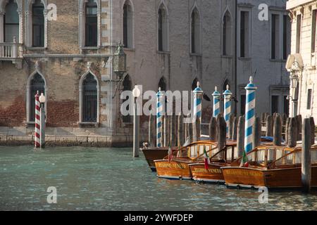 Vecchi motori di lusso in legno ormeggiati sui loro palati sul Canal grande, circondati da edifici storici. Foto Stock