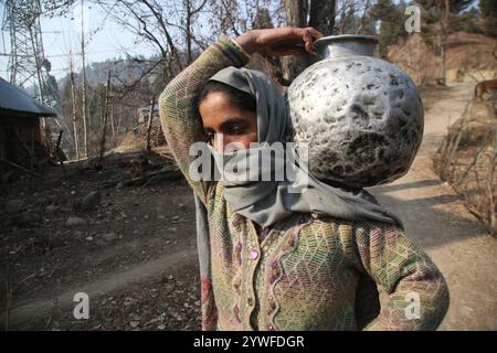 Srinagar, India. 10 dicembre 2024. Le donne di Sonabanjran, una remota zona collinare nel distretto di Pulwama del Kashmir meridionale, stanno affrontando gravi difficoltà a causa delle temperature gelide. Con l'alimentazione dell'acqua di rubinetto interrotta dal congelamento delle linee di alimentazione, i residenti sono stati costretti a raccogliere l'acqua potabile da un flusso congelato. (Foto di Nisar UL Haq Allaie/Pacific Press) credito: Pacific Press Media Production Corp./Alamy Live News Foto Stock