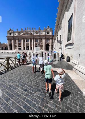 Città del Vaticano, Vaticano - 20 luglio 2022: Gruppo di turisti, compresi i bambini, cammina verso un edificio storico dall'architettura ornata sotto un chiaro trasparente Foto Stock