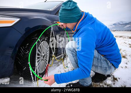 Uomo che installa catene da neve su pneumatici per auto durante l'inverno, garantendo la sicurezza su strade innevate. Foto Stock