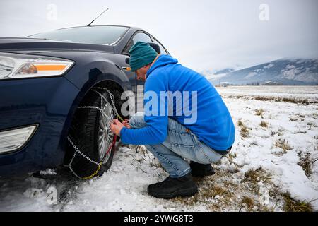 Uomo che installa catene da neve su pneumatici per auto durante l'inverno, garantendo la sicurezza su strade innevate. Foto Stock