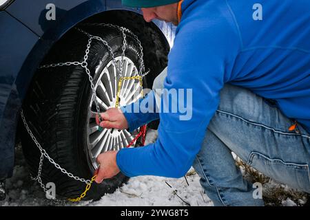 Uomo che installa catene da neve su pneumatici per auto durante l'inverno, garantendo la sicurezza su strade innevate. Foto Stock