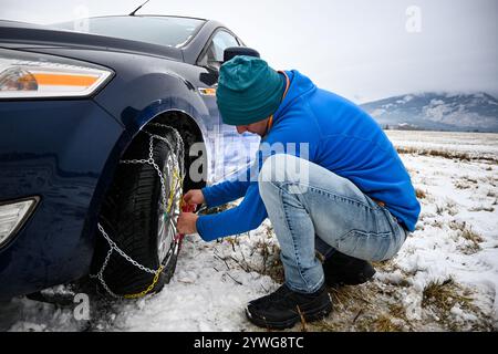 Uomo che installa catene da neve su pneumatici per auto durante l'inverno, garantendo la sicurezza su strade innevate. Foto Stock