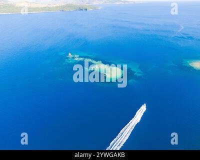 Vista aerea di una barca che naviga nelle acque azzurre vicino a una piccola isola. Foto Stock