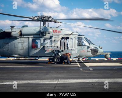 241210-N-AC395-2650 PHILIPPINE SEA (10 dicembre 2024) – Un marinaio incatena un MH-60S Sea Hawk, assegnato ai "Black Knights" di Helicopter Sea Combat Foto Stock