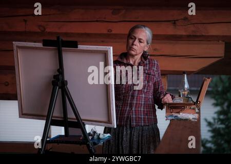 Una donna sta dipingendo un quadro su una tela. Indossa una camicia a quadri e una gonna Foto Stock