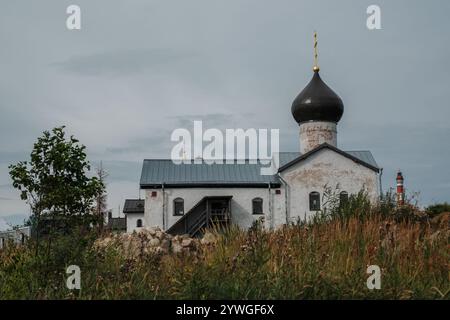 Una grande chiesa bianca con un campanile si trova in un campo. L'edificio e' circondato da erba alta e alberi. Il cielo è nuvoloso e l'atmosfera lo è Foto Stock