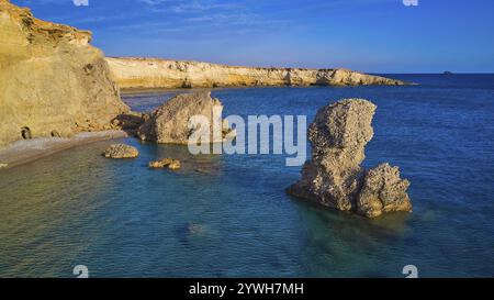 Grandi formazioni rocciose sorgono dal mare turchese sotto un cielo limpido, colpo di droni, luce serale, spiaggia di Araki, costa sud-occidentale, Karpathos, D. Foto Stock
