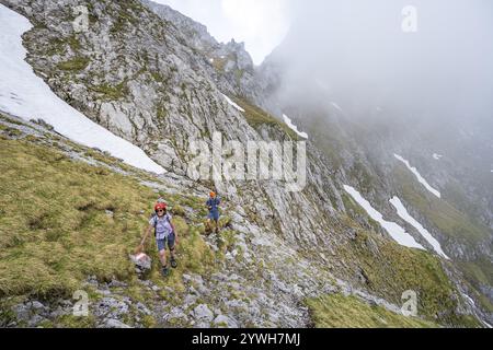 Alpinista con casco su uno stretto sentiero escursionistico, ascesa all'Ackerlspitze, nuvole che si muovono intorno alle montagne, Wilder Kaiser, Kaiser Mountains, Tyr Foto Stock