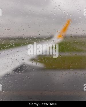 Questa foto cattura una vista giorno piovoso dalla finestra di un aereo. Le goccioline d'acqua sono sparse attraverso il vetro, creando una prospettiva morbida e sfocata Foto Stock