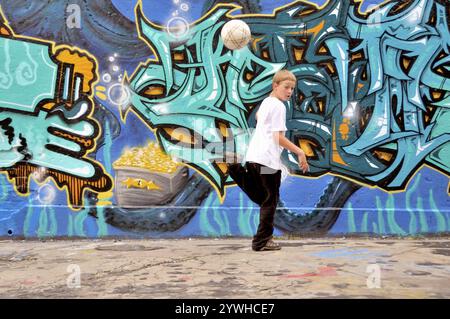 Un bambino di dieci anni gioca con il suo calcio davanti a un muro di graffiti, campo da calcio in Germania Foto Stock