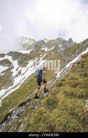 Alpinista con casco su uno stretto sentiero escursionistico, ascesa all'Ackerlspitze, nuvole che si muovono intorno alle montagne, Wilder Kaiser, Kaiser Mountains, Tyr Foto Stock