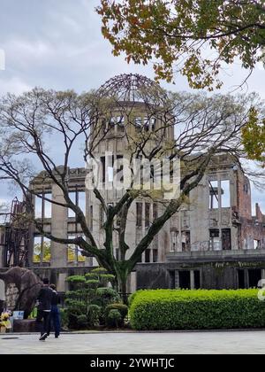 Il Memoriale della pace di Hiroshima, o Atomic Bomb Dome, sorge tra alberi e vegetazione a Hiroshima, in Giappone, con visitatori che aggiungono dimensioni e connessioni. Foto Stock