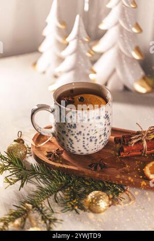 Tazza fumante di tè natalizio con fetta di arancia e spezie poggiate su un vassoio di legno Foto Stock