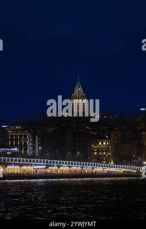 Una vista notturna mozzafiato di Istanbul con l'iconica Torre Galata illuminata contro il cielo scuro, con il vibrante Ponte Galata. Foto Stock