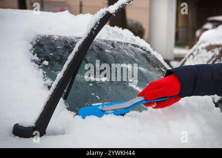 Mano di donna con spazzola e rimuovere la neve dalla vettura e dal parabrezza. Problemi invernali nel trasporto Foto Stock