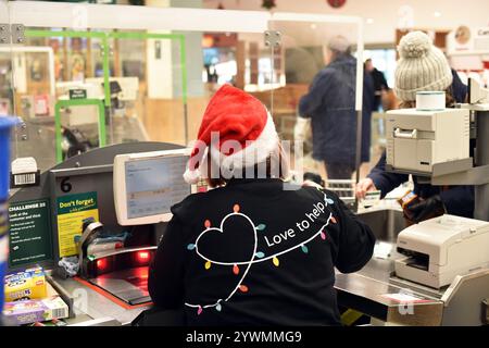 Un assistente di un supermercato lavora sulle casse a Natale con un cappello di Natale nel Regno Unito Foto Stock