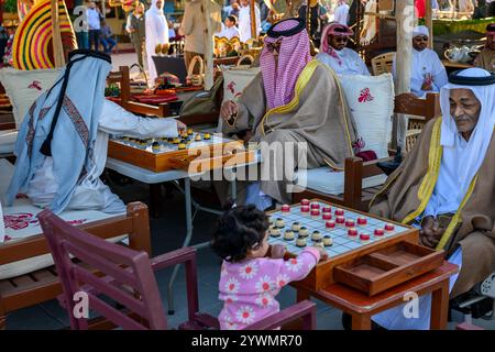 Doha, Qatar, 29 novembre 2024: Gli uomini tradizionali del Qatar giocano a un gioco da tavolo Dama sulla spiaggia di Katara durante il 14° festival tradizionale dei dhow a Karta, c Foto Stock