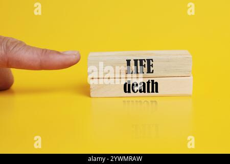 Simbolo di vita o di morte. Concetto parola vita o morte su blocchi di legno. Mano d'affari. Bellissimo sfondo giallo. Concetto di affari e di vita o di morte. Foto Stock