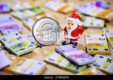 Weihnachtsmannfigur und Münze mit Eurozeichen inmitten von Geldscheinen, Symbolfoto Weihnachtsgeld *** Babbo Natale con simbolo dell'euro circondato da banconote, foto simbolica dei soldi di Natale Foto Stock