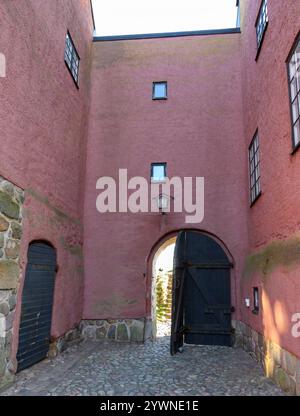 Una grande porta di legno nero si erge in modo prominente all'entrata, incorniciata da pareti rosa e pietra naturale. L'ambiente pittoresco presenta piccole finestre e una Foto Stock