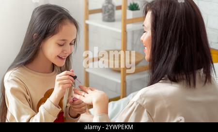 Ragazza teen felice che fa le unghie della madre, dipingendole con smalto sul letto a casa. Salone di bellezza domestico concetto Foto Stock