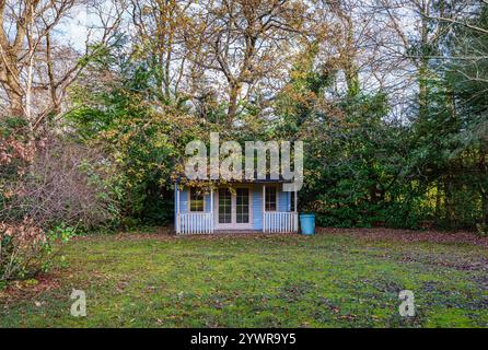 Una casa estiva blu in un giardino nel Surrey, nel sud-est dell'Inghilterra in inverno, sotto i rami di un albero di quercia (Quercus robur) con foglie cadute sul prato Foto Stock