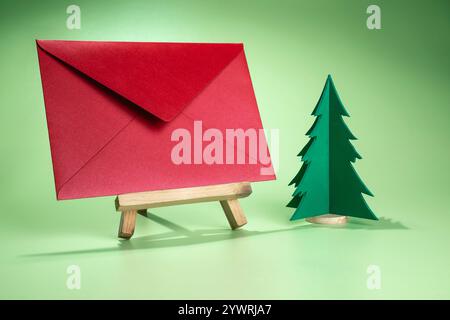 Vista ravvicinata di un albero di Natale in miniatura e busta su un cavalletto in legno con sfondo colorato. Mockup, modello vuoto, spazio di copia. Saluto o io Foto Stock