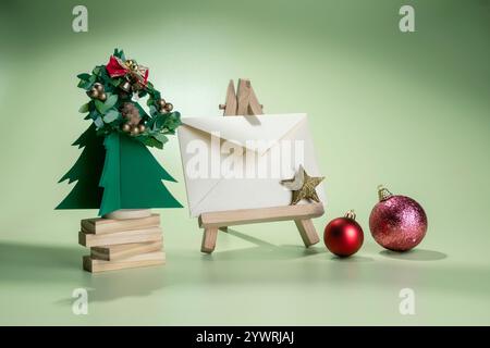 Vista ravvicinata di un albero di Natale in miniatura e ornamento natalizio con una busta su un cavalletto di legno con sfondo colorato. Mockup, modello vuoto Foto Stock