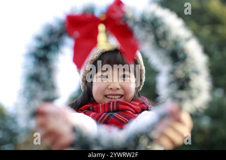 Ragazza in cappello che sbircia attraverso la corona di Natale Foto Stock