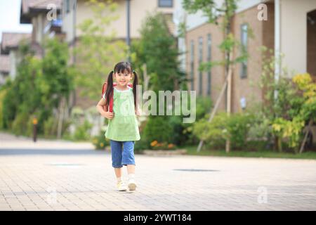 Ragazza che cammina nella zona residenziale con la borsa della scuola sulla schiena Foto Stock