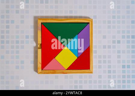 Un colorato puzzle Tangram nel suo contenitore su un tavolo di legno. Foto Stock